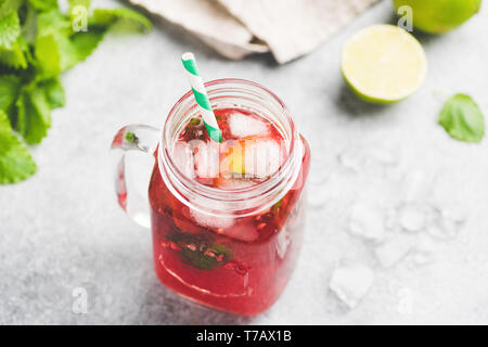 Berry Ice Tea mit Glas Schale mit grünen Trinkhalm auf konkreten Hintergrund. Erfrischend im Sommer kaltes Getränk Stockfoto