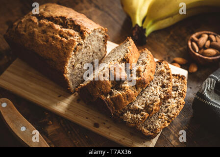 Banana Bread Loaf in Scheiben geschnitten auf hölzernen Tisch. Vollkorn Bananenkuchen mit Muttern Stockfoto