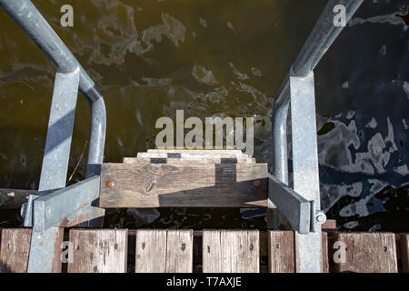 Eine metallleiter an einer hölzernen Pier. Abstieg in das Wasser am See. Frühling. Stockfoto