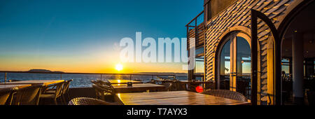 Panoramablick leer Sommer Terrasse mit Tischen und Stühlen im Restaurant an der Küste in malerischen Sonnenuntergang über dem Mittelmeer Se Stockfoto