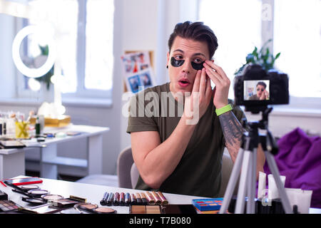 Genaue ausdrucksstarke jungen Kerl Anwendung schwarzes Auge Patches Stockfoto