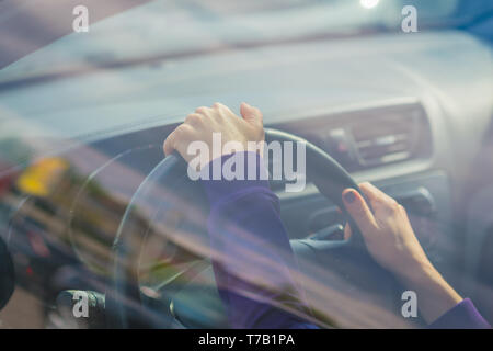 Die junge Frau Hand auf schwarzes Lenkrad während der Fahrt im Auto. Blick von außen auf das Auto. Stockfoto