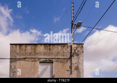 Braun verwitterte Fassade eines Hauses. Blick auf seine Oberseite mit einer Antenne, Laterne und ein Netz von Kabeln. Bewölkter Himmel. Arico Viejo, Teneriffa, Kanarische Inseln, Stockfoto