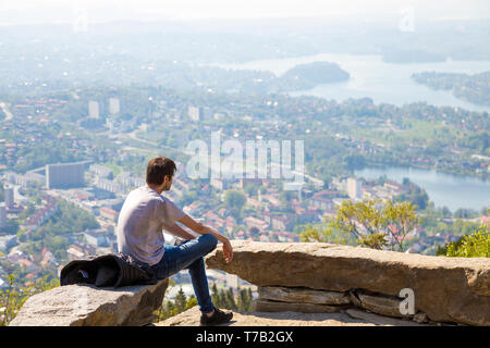 Mann allein sitzen, Musik hören, bei herrlicher Aussicht über Bergen, Norwegen von ulriken Berg suchen Stockfoto