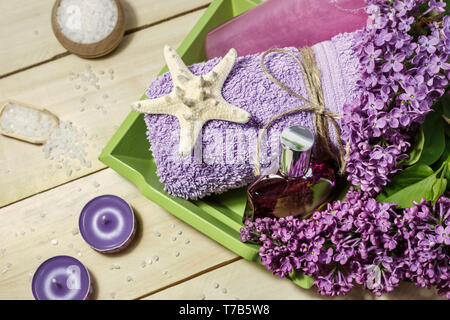 Spa-Konzept mit Meersalz, Parfüm, Kerzen, Handtuch und lila Blumen für Badewanne auf Holz- Hintergrund. Aromatherapie für Entspannung, Ansicht von oben. Stockfoto