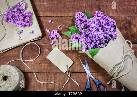 Nahaufnahme von Geschenk- und Strauß Flieder in Kraftpapier auf einer hölzernen Hintergrund gewickelt. Stockfoto