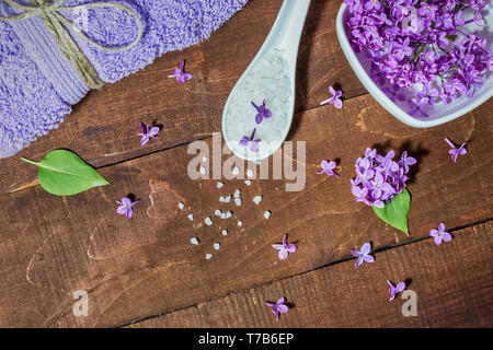 Spa und Wellness Komposition mit duftenden, violetten Blüten Wasser in der Schüssel, Meersalz und Handtuch auf Holz- Hintergrund. Aromatherapie für Entspannung, Ansicht von oben Stockfoto