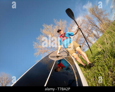 Senior Paddler tragen aufblasbare Rettungsweste und paddeln Handschuhe ist sein Stand up paddleboard am See starten, POV Bild mit Action Kamera Breite ein Stockfoto