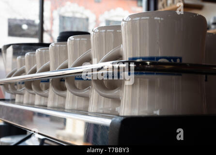 Nahaufnahme einer Reihe von sauberen, weißen und blauen Kaffeetassen hinter einem Chrom Schiene. Mit einer geringen Tiefenschärfe fotografiert. Stockfoto