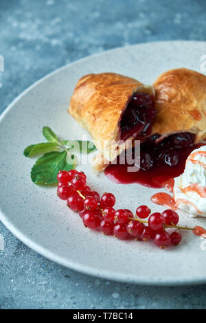 In Scheiben geschnittene Hausgemachte berry Strudel mit frischen rote Johannisbeere Beeren und Puderzucker auf einem alten Hintergrund auf einer Platte mit Eis pic serviert. Stockfoto