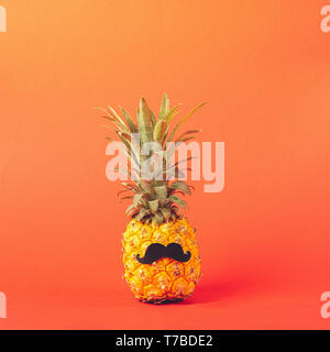 Gelb reife Ananas mit schwarzen Schnurrbart auf einem roten Hintergrund. Lustiges Gesicht von einem tropischen Früchte. Konzept kopieren. Stockfoto