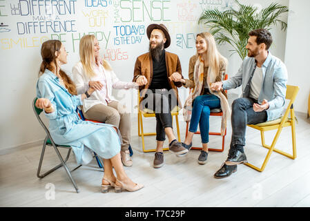 Junge Menschen halten sich an den Händen zusammen während der psychologischen Therapie, Meditation und gemeinsam lösen einige mentale Probleme im Büro Stockfoto