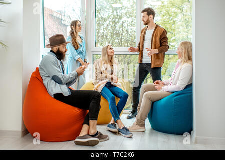 Gruppe von verschiedenen Leuten ein Gespräch in der Kaffeepause auf dem bunten Hocker in der Nähe der Fenster im Büro Stockfoto