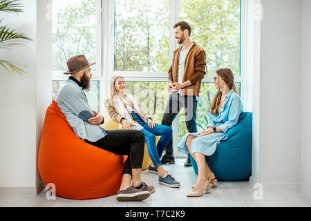 Gruppe von verschiedenen Leuten ein Gespräch in der Kaffeepause auf dem bunten Hocker in der Nähe der Fenster im Büro Stockfoto