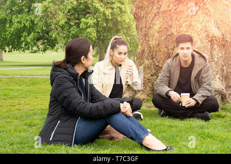 Familie mit zwei Kindern in Kaffee sitzen auf Gras im Park zu plaudern. Stockfoto