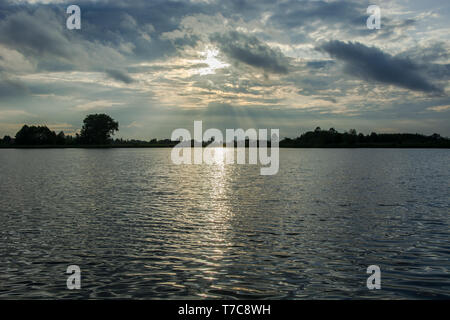 Die Sonne hinter Wolken und Regen reflektierende Licht im Wasser des Sees - Abendlicher Blick in Stankow, Lubelskie, Polen Stockfoto