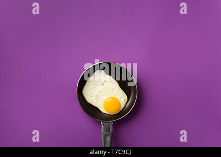 Kreative essen Konzept mit Spiegelei auf Schwenk über violett unterlegt. Ansicht von oben. Kreative Muster im minimalistischen Stil. Flach. Stockfoto