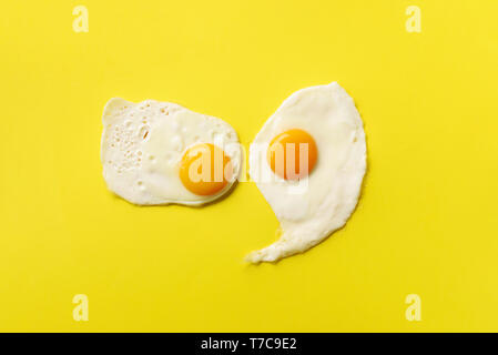 Zwei Spiegeleier auf gelbes Papier Hintergrund. Kreative essen Konzept im minimalistischen Stil. Ansicht von oben. Stockfoto