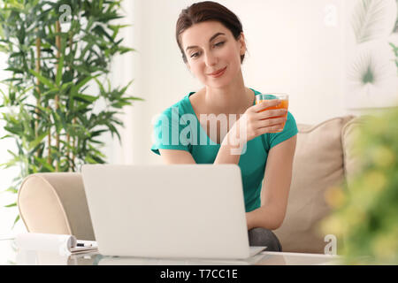 Junge weibliche Freiberufler Saft trinken während der Arbeit mit dem Laptop zu Hause Stockfoto