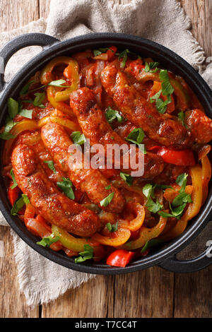 Traditionelle gegrillte Würstchen mit buntem Paprika, Zwiebeln und Tomaten close-up in einer Pfanne auf dem Tisch. Vertikal oben Ansicht von oben Stockfoto