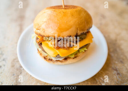 Selbstgemachte Cheeseburger mit frischem Gemüse, frische leckere Burger mit Käse, Gurken, Tomaten, karamellisierten Zwiebeln und Salat Stockfoto