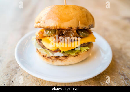 Selbstgemachte Cheeseburger mit frischem Gemüse, frische leckere Burger mit Käse, Gurken, Tomaten, karamellisierten Zwiebeln und Salat Stockfoto