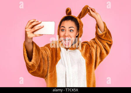 Junge Frau in Bunny kigurumi steht auf rosa Hintergrund unter selfie Bild auf dem Smartphone zu schreien Kamera schließen aufgeregt isoliert - oben Stockfoto