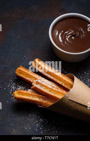 Churros in Papiertüte mit Zucker und Schokolade Soße auf dunklen schwarzen Hintergrund Stockfoto