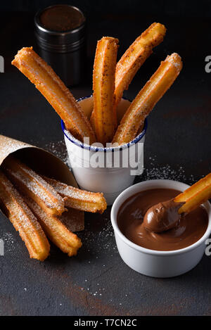 Churros mit Zucker und Zimt in geschmolzene Schokolade tauchen Stockfoto