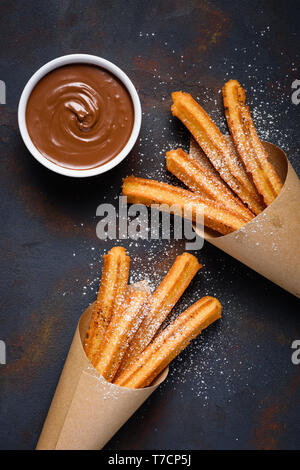 Gebratene traditionelle churro Sticks mit Zucker Pulver Zimt und Schüssel von Schokolade dip auf dunklen Tabelle Ansicht von oben Stockfoto