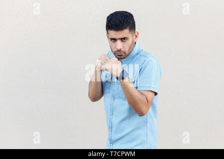 Porträt von Ernst gut aussehender Junge Bartgeier Geschäftsmann in blaues Hemd mit Boxing Fäuste und zum Angriff bereit und Kamera. indoor Stud Stockfoto