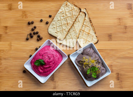 Raw Vegan essen. Schwarze Bohnen Hummus und Rote Beete Hummus mit gerösteten Cracker in einem hölzernen Textur Hintergrund Stockfoto