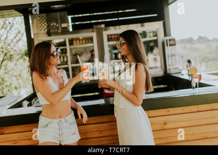 Zwei hübsche junge Frauen trinken Cocktails und Spaß am Pool im heißen Sommer Tag Stockfoto