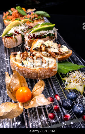 Vorspeise Bruschetta mit Käse, Honig, Nussbaum und anderen Zutaten auf schwarzem Hintergrund. Close-up. Italienisches Essen. Stockfoto