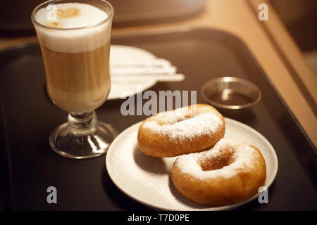 Auf das Fach ein köstliches Frühstück mit einer belebenden Kaffee trinken und zwei Donuts bestreut mit Puderzucker, gibt es einen Container mit Chocola Stockfoto