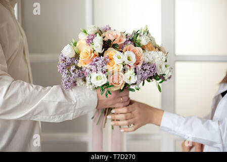 Man streckt seine Hände und gibt einen großen Blumenstrauß aus Rosen und Flieder vor dem Hintergrund einer Glasfenster isoliert. Clos Stockfoto