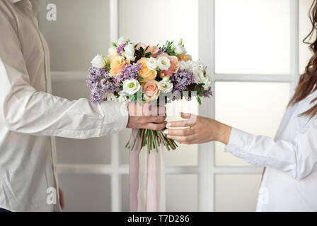 Man streckt seine Hände und gibt einen großen Blumenstrauß aus Rosen und Flieder vor dem Hintergrund einer Glasfenster isoliert. Clos Stockfoto