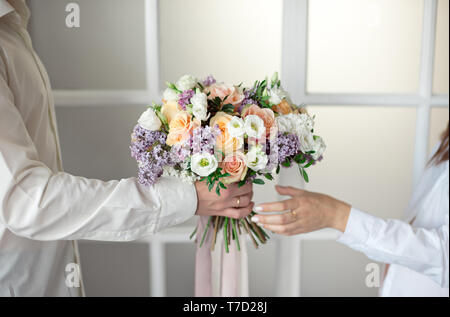 Man streckt seine Hände und gibt einen großen Blumenstrauß aus Rosen und Flieder vor dem Hintergrund einer Glasfenster isoliert. Clos Stockfoto