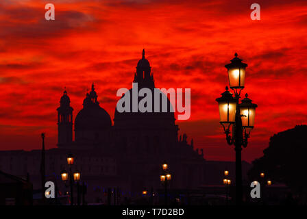 Geheimnisvolle Blut rot Sonnenuntergang über Salute Basilika (Saint Mary für Gesundheit) Kuppeln mit alten Straßenlaternen in Venedig Stockfoto