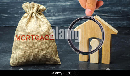 Ein Beutel mit Geld und das Wort Hypothek und ein Holzhaus mit einem Mieter. Die Anhäufung von Geld Zinsen auf Hypotheken zu bezahlen. Kauf eines ordnungsgemäßen Stockfoto