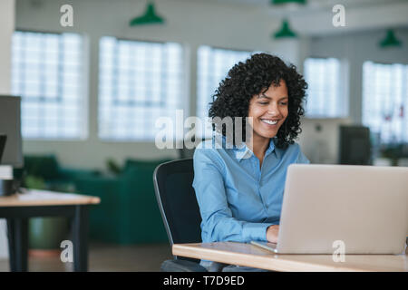 Lächelnden jungen Geschäftsfrau, die an einem Notebook arbeitet an ihrem Schreibtisch Stockfoto