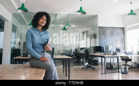 Lächeln, Geschäftsfrau, sitzen auf einem Büro tisch Holding ein Tablet Stockfoto