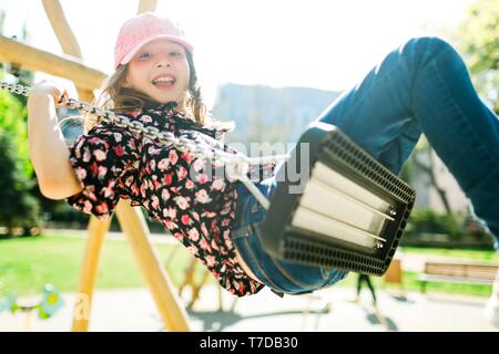 Lächelnd Kind in Rosa cap Schwingen auf Spielplatz - Sonniger Tag und unbeschwerte Kindheit Stockfoto