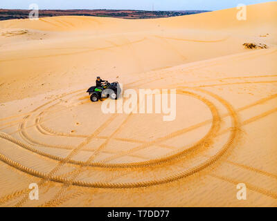 Eine touristische Männer auf einem Quad Bike Fahrten um auf einer Sanddüne in der Wüste von Mui Ne, Vietnam. Stockfoto