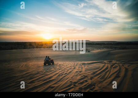 Sonnenaufgang in der Wüste. Szene mit zwei ATV Biker. Touristen fahren mit einem Off-road-ATV durch die Sanddünen der Vietnamesischen Wüste. Safari in den frühen Mo Stockfoto
