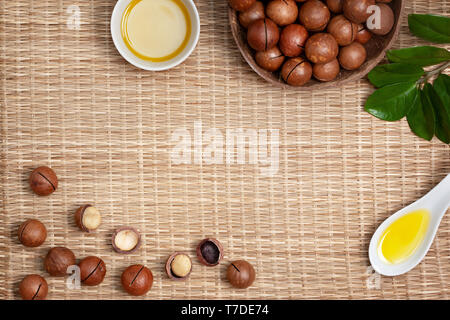Macadamia Nüsse in einer Schüssel, macadamiaöl in einer weißen Schüssel auf einen Strohhalm (Bambus) Hintergrund. Ansicht von oben Stockfoto