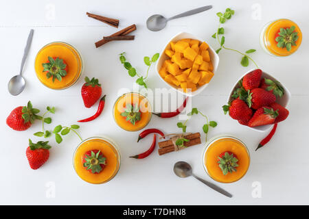 Traditionelle italienische süßes Dessert Panna cotta mit Mango Gelee mit Hauch von red hot chili Piri-Piri in Töpfen auf weissem Holztisch und embellis serviert. Stockfoto