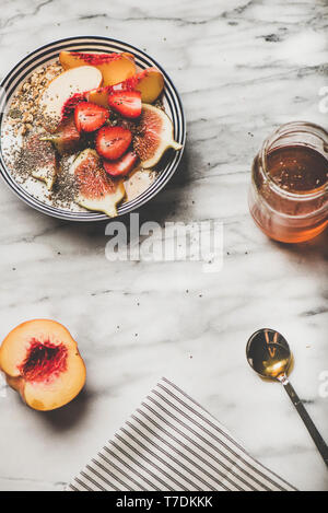 Gesund Sommer Frühstück. Flachbild-lay der griechischen Joghurt Müsli Schüssel mit Erdbeeren, Feigen, Pfirsich, Chia Samen und Honig über Marmor Hintergrund, oben vie Stockfoto