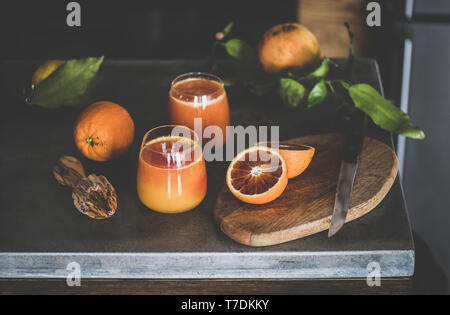 Zwei Gläser frisch gepressten Orange Saft oder Smoothie und frische Früchte auf Beton Arbeitsplatte in der Küche. Gesunder Lebensstil, vegan, Vegetarisch, Alk Stockfoto
