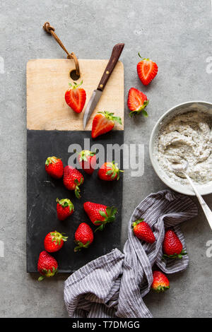 Vorbereitung von Chia Milchreis mit frischen Erdbeeren auf schwarzem Marmor Brett über grauer Beton Hintergrund Stockfoto